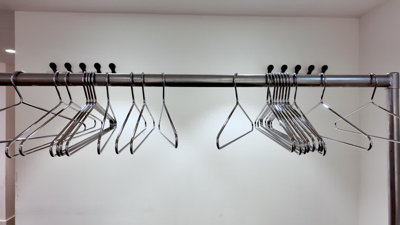 Appendino in metallo con grucce in filo d'acciaio vuote su parete bianca, esposizione al dettaglio, organizzazione guardaroba, lavanderia, ripostiglio e industria della moda