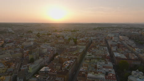 Aerial-slide-and-pan-footage-of-famous-Basilica-di-Santa-Maria-Maggiore.-Fly-above-blocks-of-apartment-buildings-in-urban-borough.-Panoramic-view-against-sunset.-Rome,-Italy