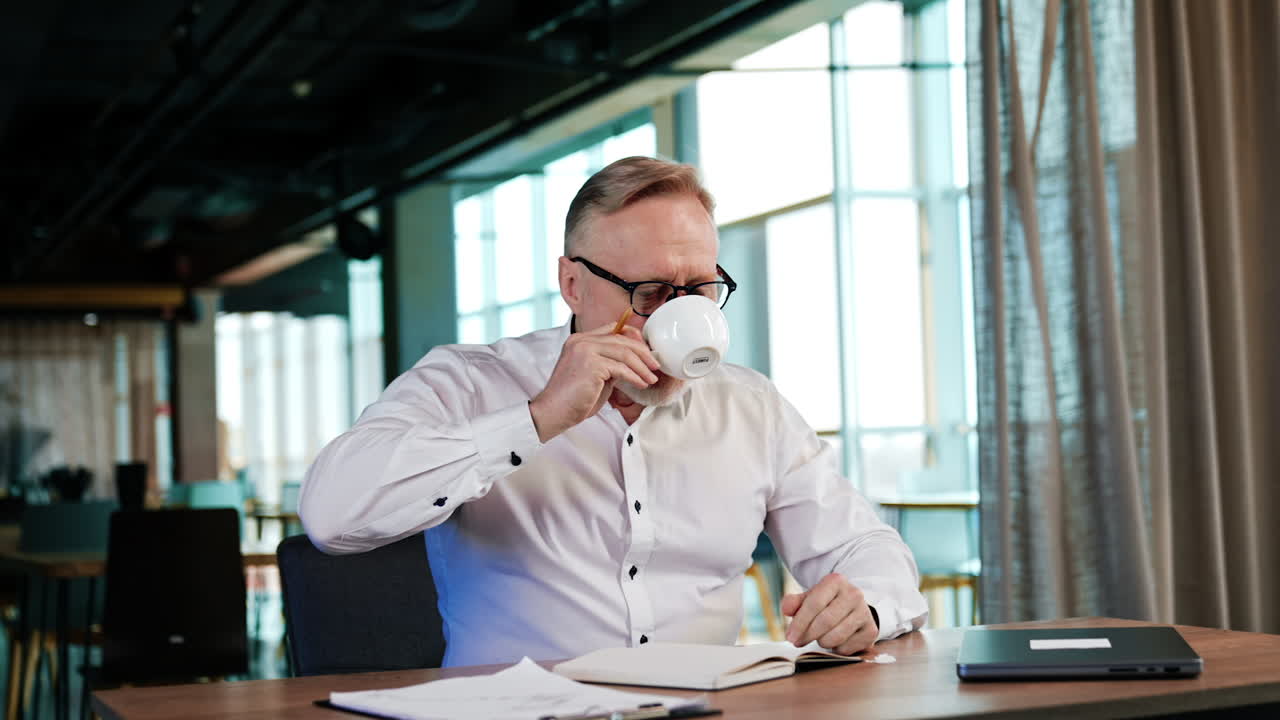 Hard-working businessman taking a sip of coffee not distracting from his duties. Pensive man drinks and puts his cup continuing work.