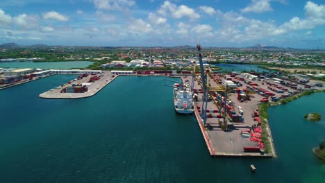 Puerto-De-Contenedores-De-Envío-En-La-Isla-De-Curacao,-Drone-Descender-Inclinado-Hacia-Arriba,-Día-De-Cielo-Azul