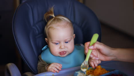 blue-eyed blond baby is given food from spoon. mother feeding her child with healthy vegetables.