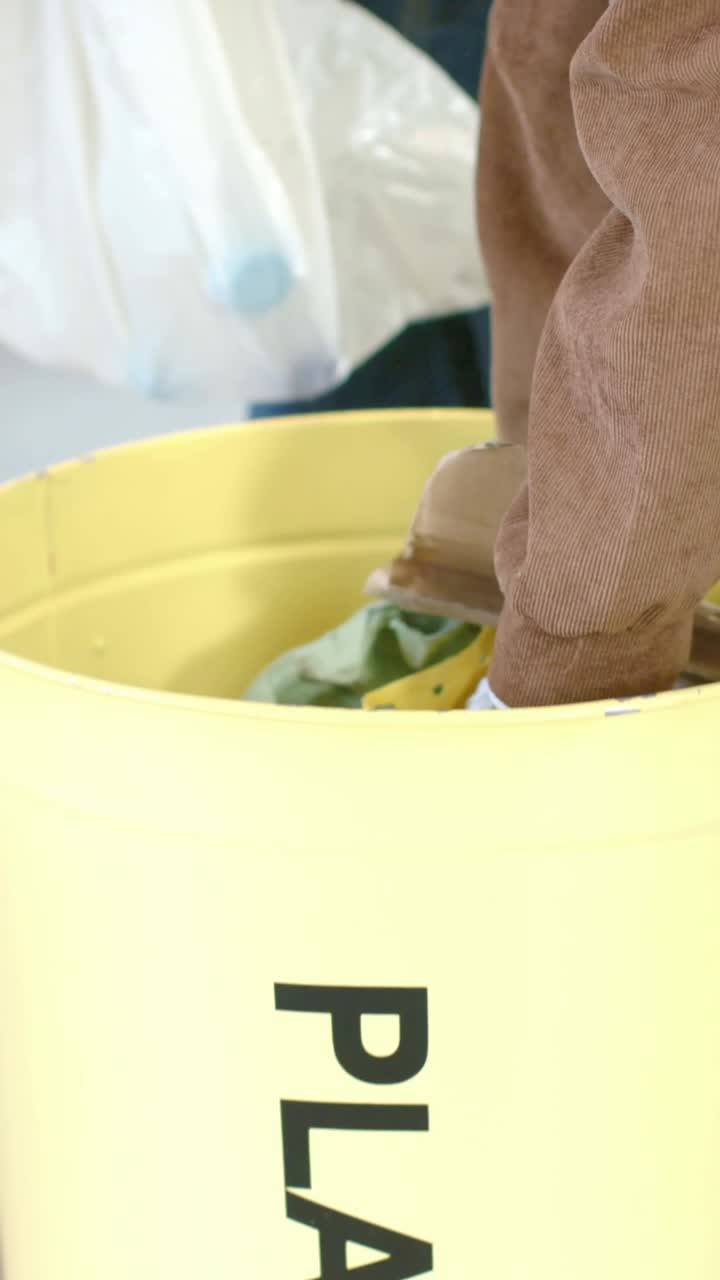 Vertical video: Walking to yellow PLAST bin, child in brown jacket recycling egg carton, copy space