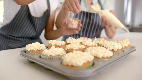 decorating cupcakes with sprinkles, two people enjoying baking activity at home