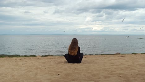 woman meditating on a beach, watching the seagulls