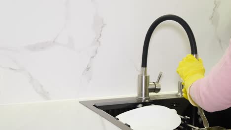 a woman in gloves washes a dishes a spoon in a modern white kitchen