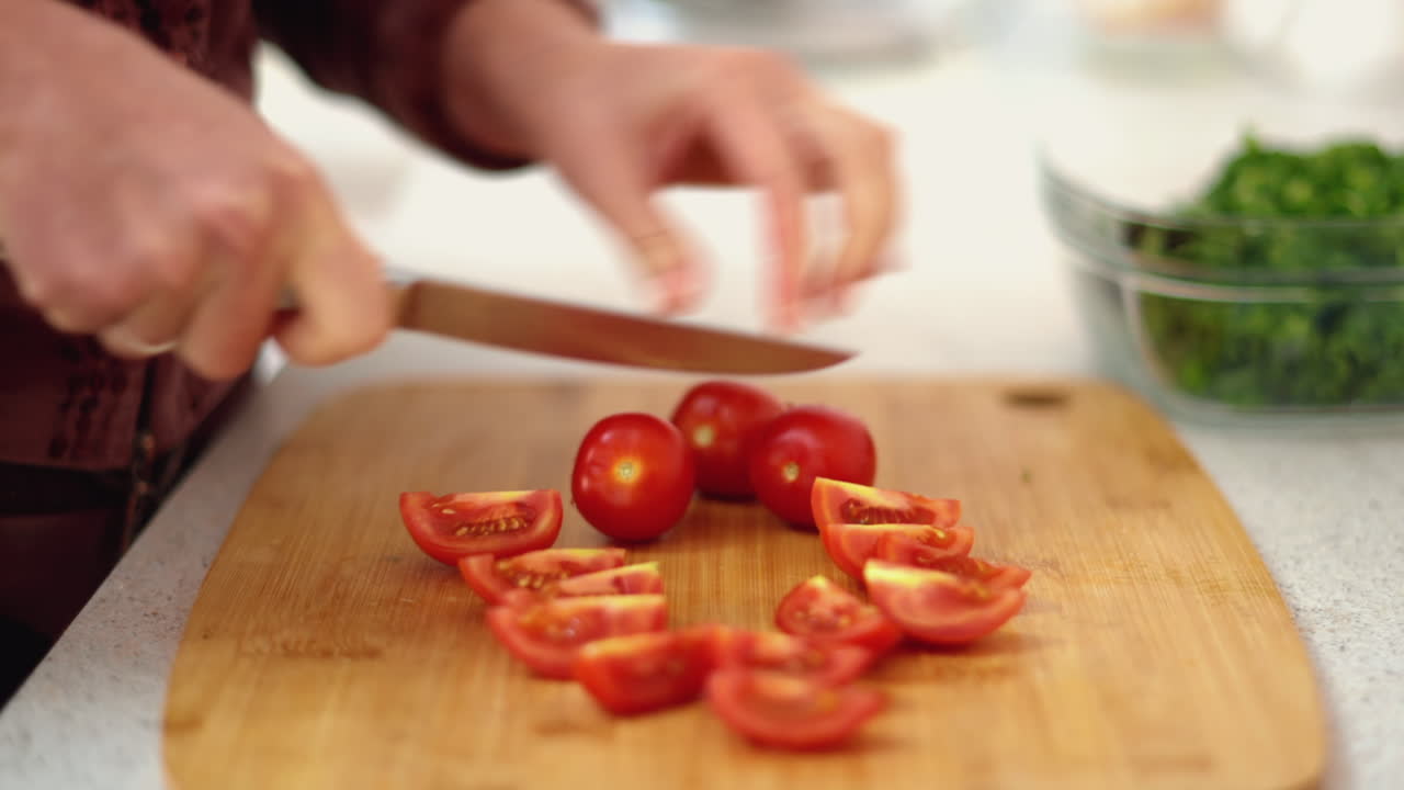 Close up of a woman cutting up cherry tomatoes on a wooden board
