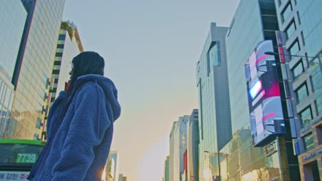 hermosa modelo de mujer asiática oriental en una gran ciudad urbana con gafas de sol y actos de teléfono celular frente a los rascacielos