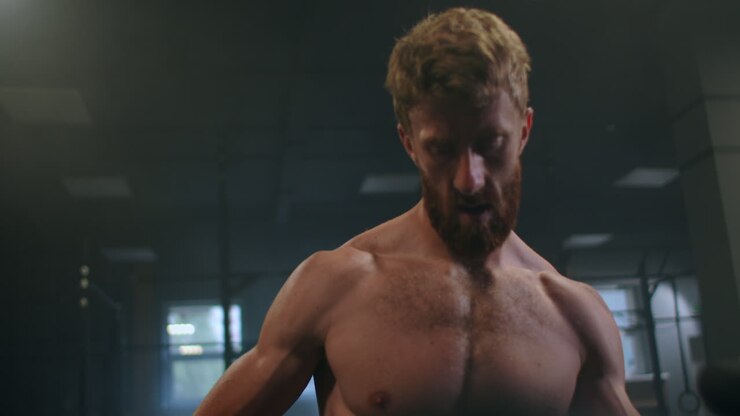 Close-up: a tenacious purposeful male athlete pushes a heavy sled in the gym. exercise with a heavy weight for endurance. Sports spirit of victory