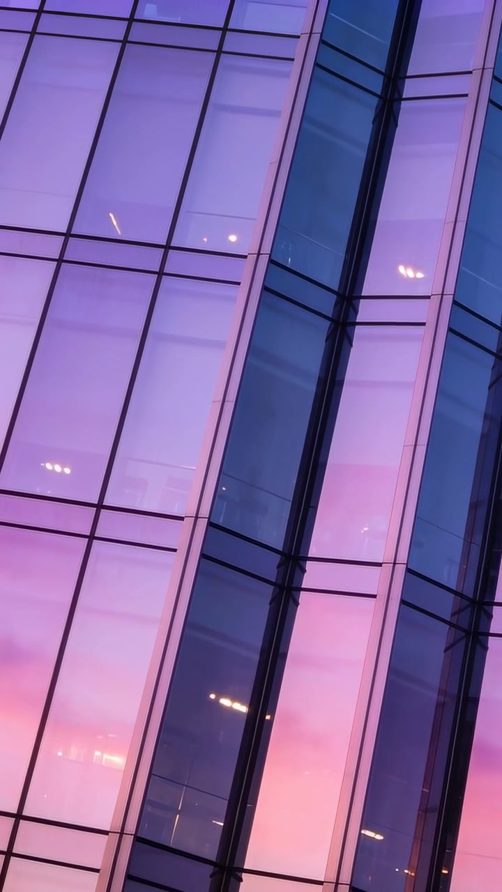 Vídeo vertical: Câmera em movimento fazendo a fachada refletir o brilho do pôr do sol na torre, mostrando as luzes da baía.