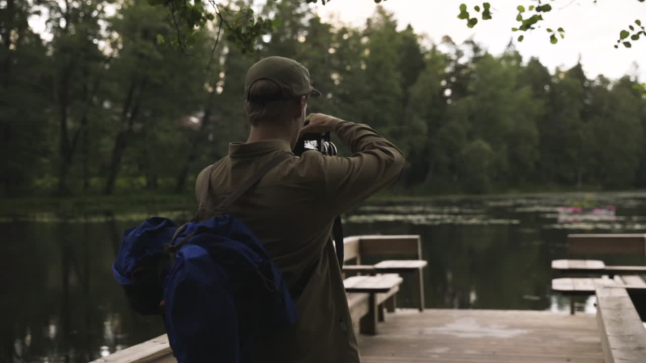 Pan of male photographer taking pictures of lake from wooden bridge