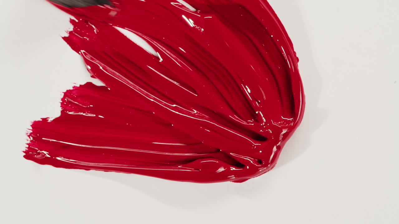 Paintbrush Spreading Vibrant Red Paint on White Surface