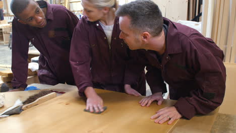 carpenter with apprentices finishing wood in workshop