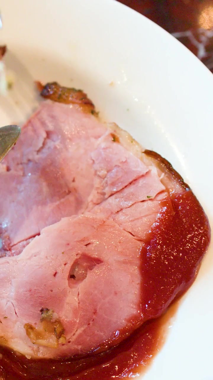 Zbliżenie na nóż i widelec krojące pieczoną szynkę podaną z grillowaną papryką.
