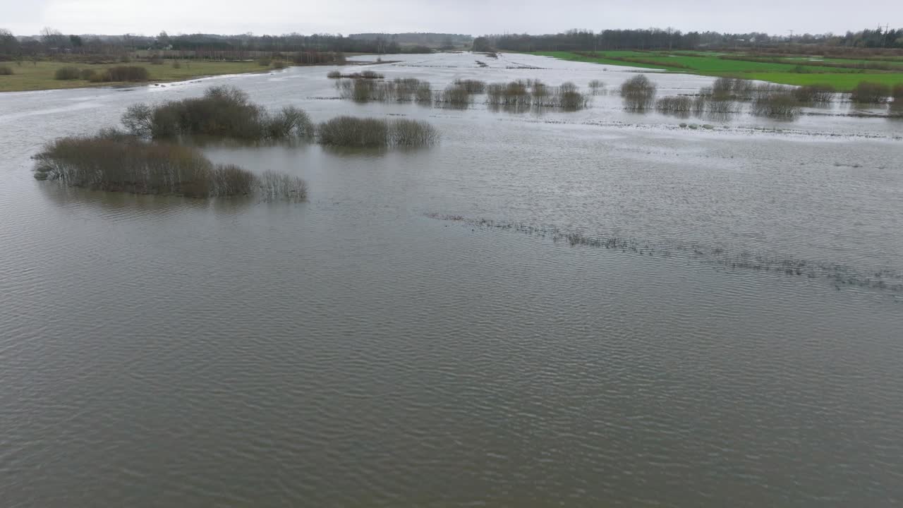 Aerial establishing view of high water in springtime, Alande river flood, brown and muddy water, agricultural fields under the water, overcast day, wide drone shot moving forward low