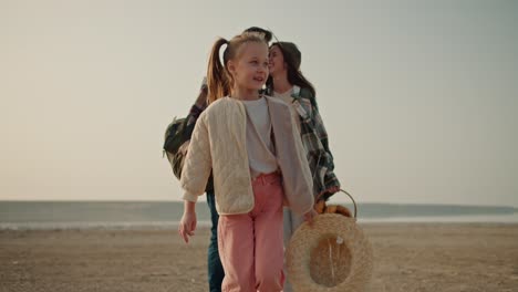 A-little-blonde-girl-in-a-white-jacket-and-pink-pants-walks-along-a-deserted-path-and-behind-her-are-her-parents,-a-brunette-man-and-a-brunette-girl-in-a-Green-checkered-shirt-who-carries-a-basket-of-food-during-their-picnic-outside-the-city