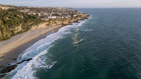 Schöne-Luftaufnahme-Von-Tausend-Schritten-Beach,-Laguna---Kalifornien,-Fliegen-über-Den-Ozean-Mit-Gebäuden-Und-Bäumen-Auf-Klippen