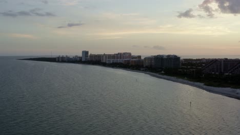 Left-rotating-aerial-drone-shot-of-the-beautiful-tropical-beach-coastline-surrounded-by-palm-trees-and-resorts-on-Crandon-Park-in-Key-Biscayne-outside-of-Miami,-Florida-on-a-warm-sunny-summer-evening