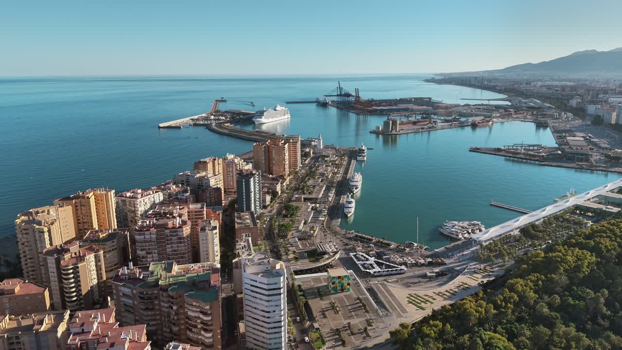 Aerial view of the Port of Málaga, Spain, showing the waterfront promenade, marina with yachts, cruise ship dock, and the coastline stretching toward the horizon
