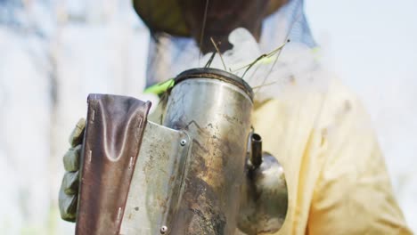 caucasian male beekeeper in protective clothing preparing smoker