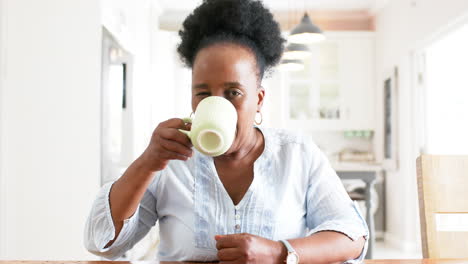 Afroamerikanische-Seniorin,-Die-Einen-Videoanruf-Macht-Und-In-Einem-Sonnigen-Zimmer-Aus-Einer-Tasse-Trinkt,-Zeitlupe