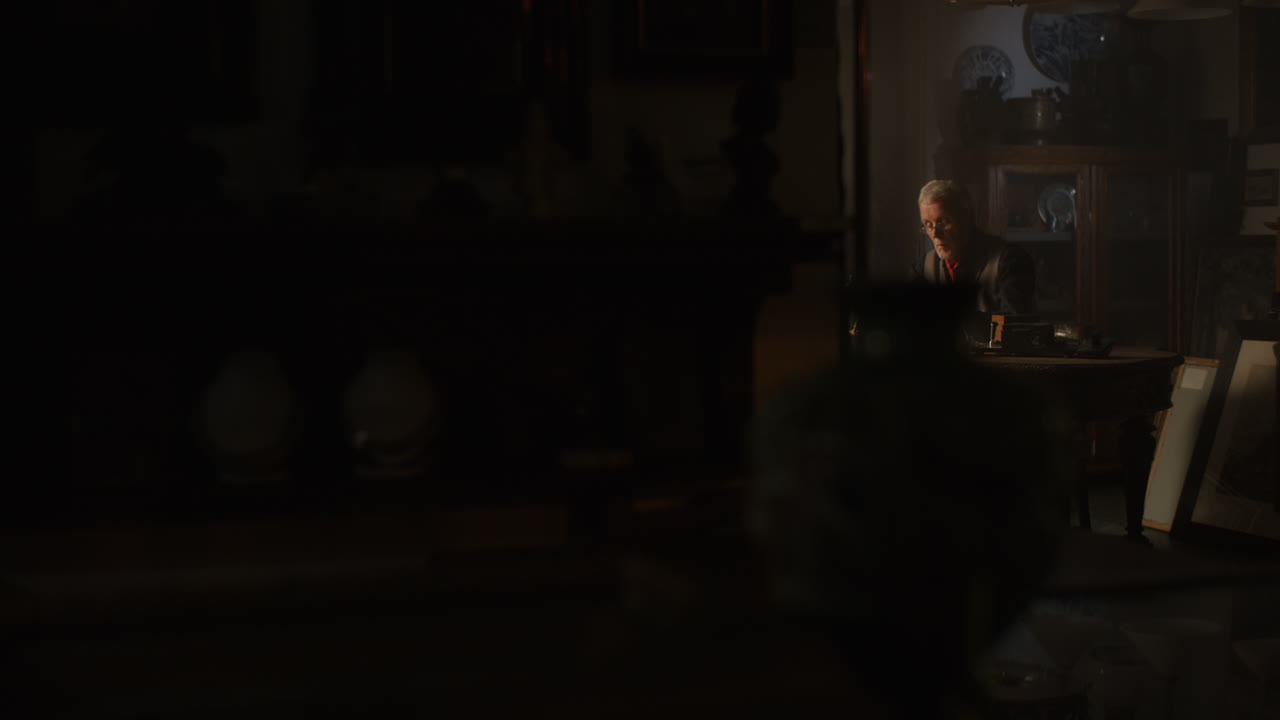 Older passionate man evaluates an old watch in his office at night