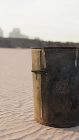 a rusty metal trash can sitting on a beach.