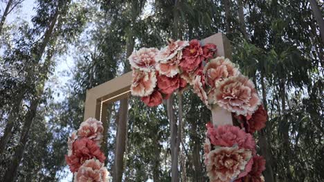 arco floral al aire libre adornado con flores rosadas suaves y corales enmarcadas por altos eucaliptos