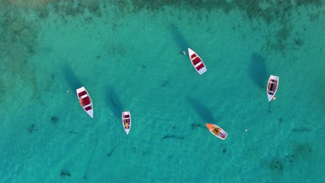 Drone-Aéreo-Estático-De-Arriba-Hacia-Abajo-De-Barcos-De-Pesca-Blancos,-Rojos-Y-Naranjas-Anclados-En-Aguas-Cristalinas-Y-Arenosas-Con-Hermosas-Sombras-En-El-Agua