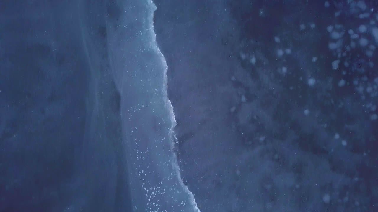 Aerial birdseye view of frozen lake Liepaja during the winter, blue ice with cracks, dry yellowed reed islands, overcast winter day, wide drone shot moving forward