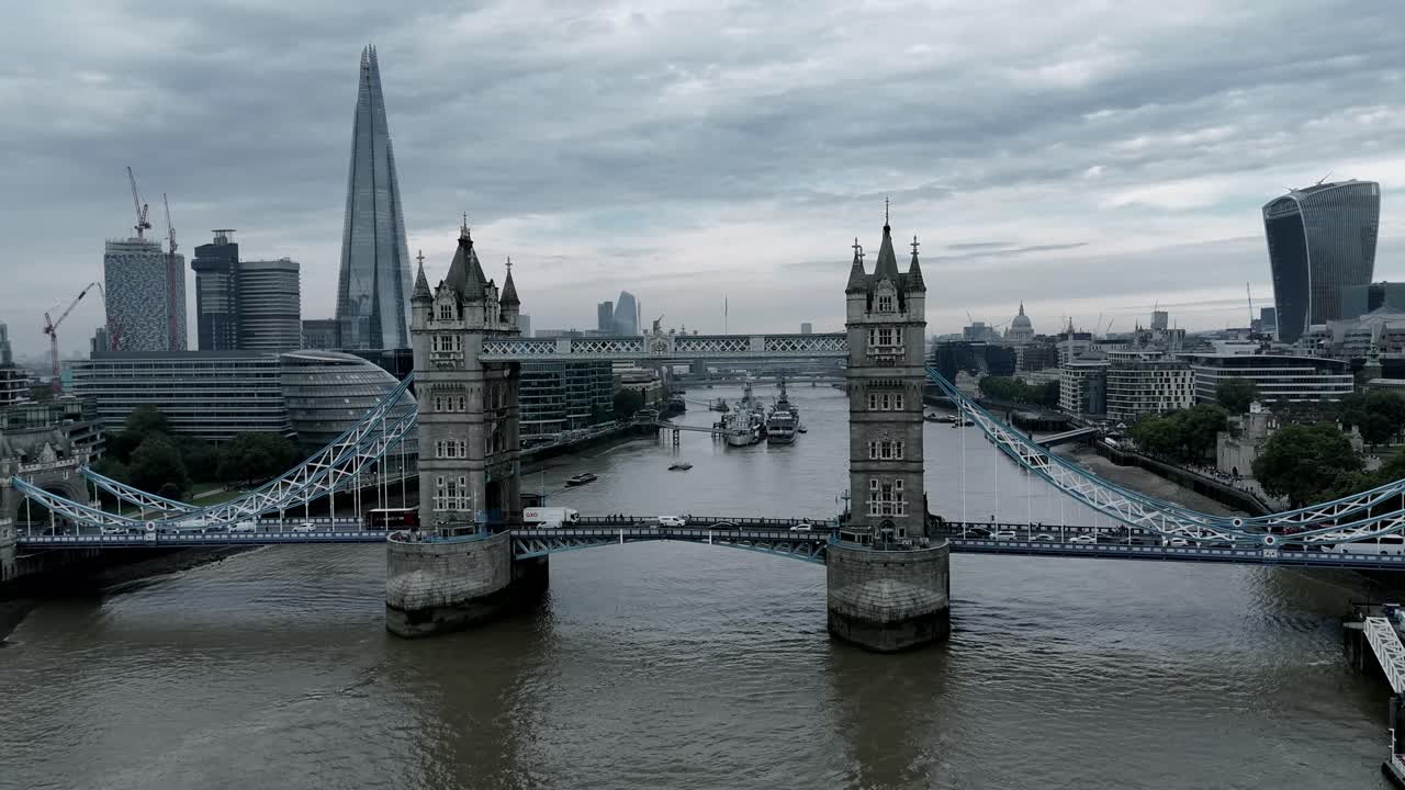 A dark, eerie aerial pan of London's iconic Tower Bridge shrouded in gloom. A raven from the Tower of London flies past, as the modern skyline looms over the shadowy, historic structures below.