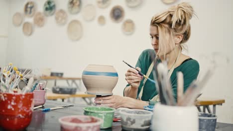 woman potter painting ceramic pot with brush at art workshop, slow motion