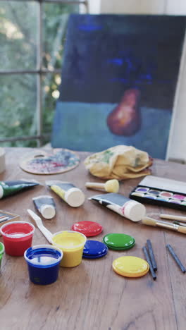 vertical video of close up of tubes and tubs of paint and brushes on table in studio, slow motion
