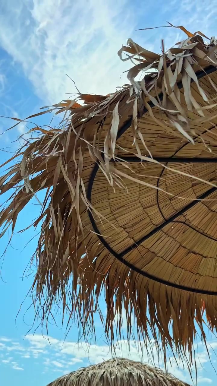 En stråparasol, der svajer på stranden under en klar blå himmel midt på en solskinsdag