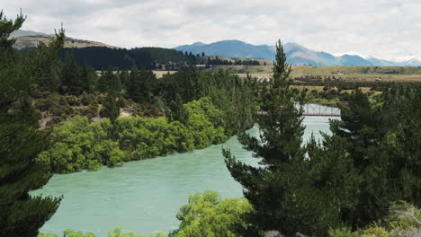 Un-Coche-Cruza-Un-Río-En-Un-Pequeño-Puente-En-El-Pintoresco-Paisaje-De-Nueva-Zelanda