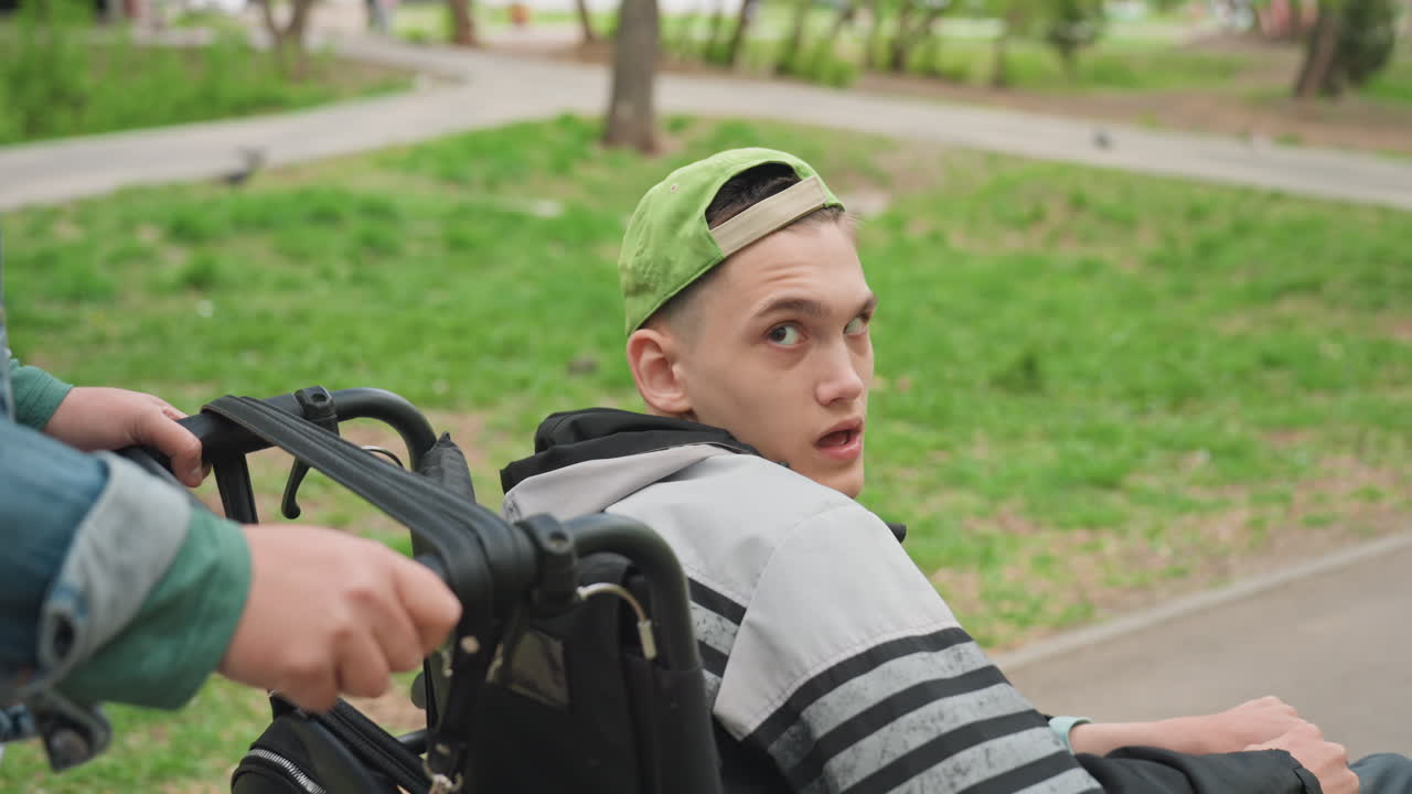 Compassionate Woman Escorts Teen Along Peaceful Outdoor Walkway In City, Tenderhearted Woman Carefully Pushes Young Person In Wheelchair Through Scenic Park Pathway With Attentive Gaze