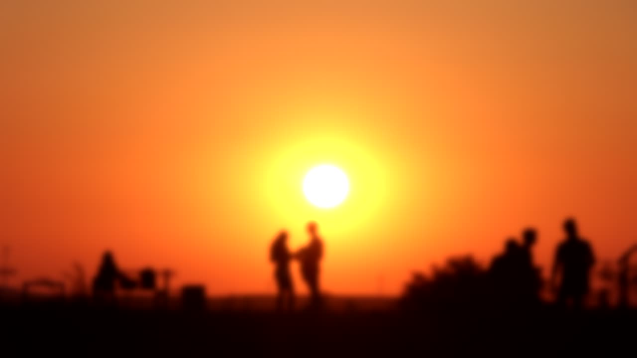 Silhouette of people watching bright orange sunset, soft focus time lapse