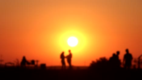 silhouette of people watching bright orange sunset, soft focus time lapse