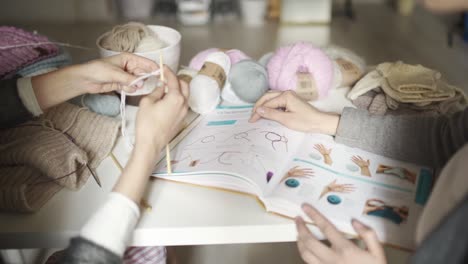 Two-creative-woman-friends-using-book-with-knitting-pattern.-Knitting-hands