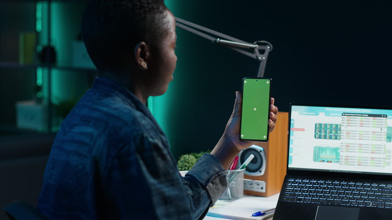 Person Looking at a Green Screen Smartphone in Front of a Laptop