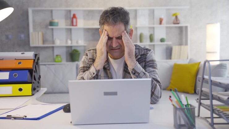 Mature man working in home office has a headache.
