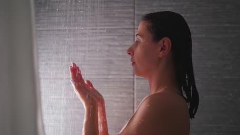 mujer sostiene las manos bajo las gotas de ducha en el baño. dama soñadora lava las palmas con agua caliente clara en el baño de casa. mujer bonita se baña por la mañana