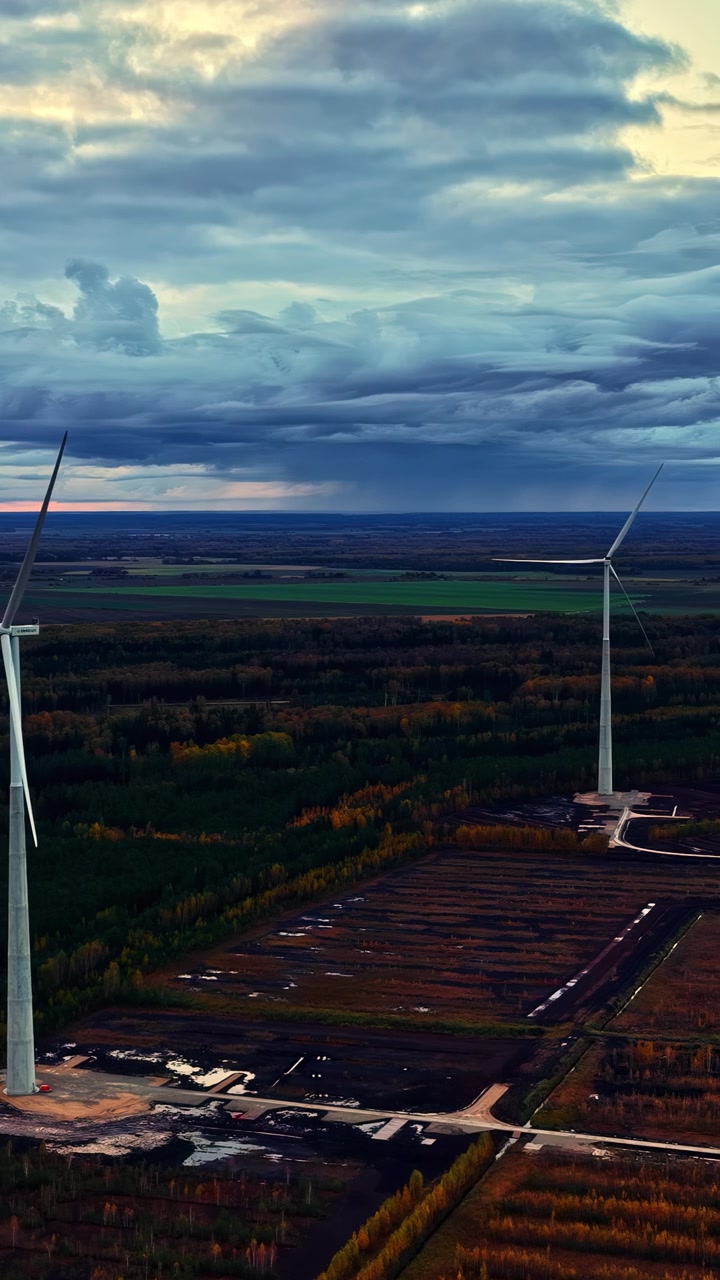 Vista aerea che scivola oltre le turbine eoliche in aperta campagna con nuvole serali suggestive