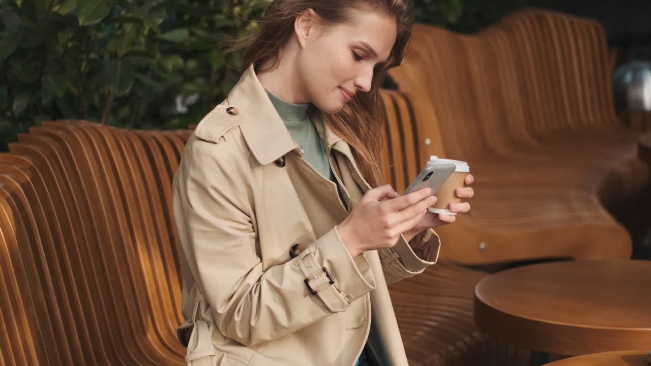 кавказская студентка использует смартфон и пьет кофе на открытом воздухе.