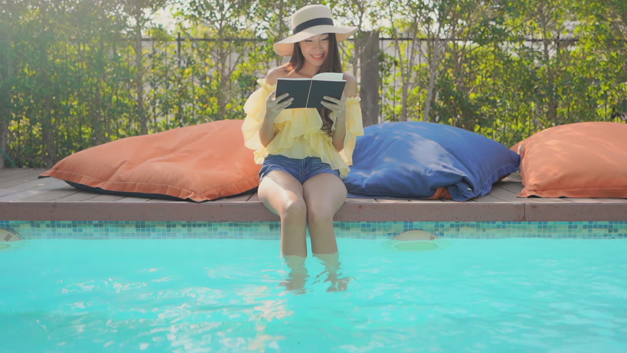 Young girl enjoys book by swimming pool dangling her feet on vacation