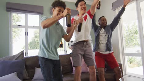 happy diverse male friends watching tv and drinking beer in living room