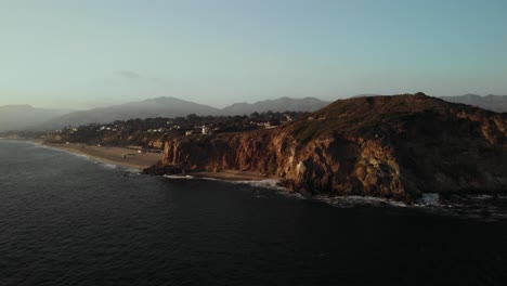 An-Aerial-Shot-of-the-Point-Dume-Cliffs-in-Malibu-in-California-as-the-Waves-Crash-Against-the-Rocks-on-a-Calm-Evening-as-the-Vibrant-Sun-Sets