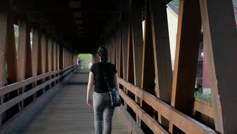 A-girl-walks-through-a-covered-bridge,-away-from-the-camera-providing-a-perspective-of-length