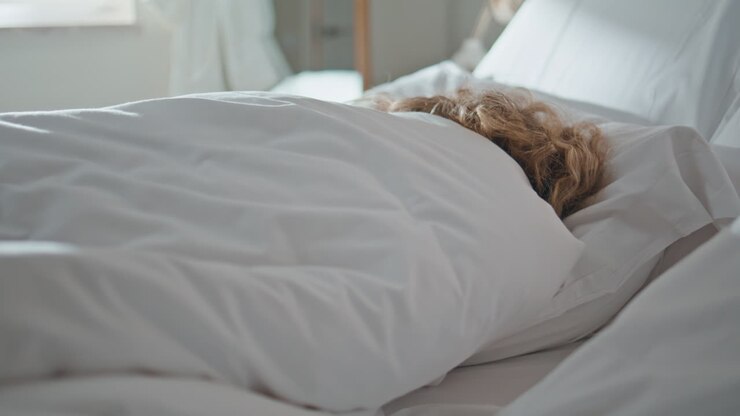 Rolig kvinde sover på pude om morgenen. Ubkymret doven pige gemmer sig under tæppet.