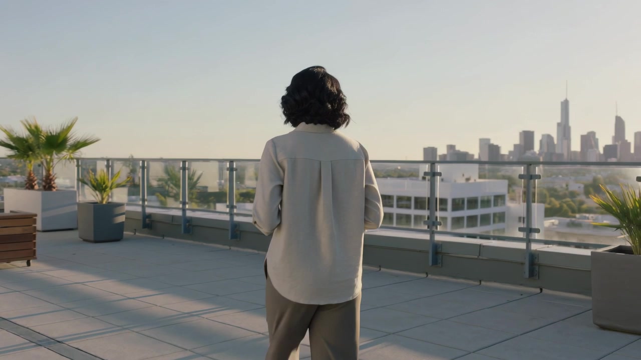 Starting profile, woman wearing shirt holding cup, turning to railing, surveying skyline on rooftop