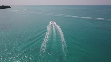 bermuda rising drone shot of a motor boat sailing out towards the open ocean with jet skis in the distance